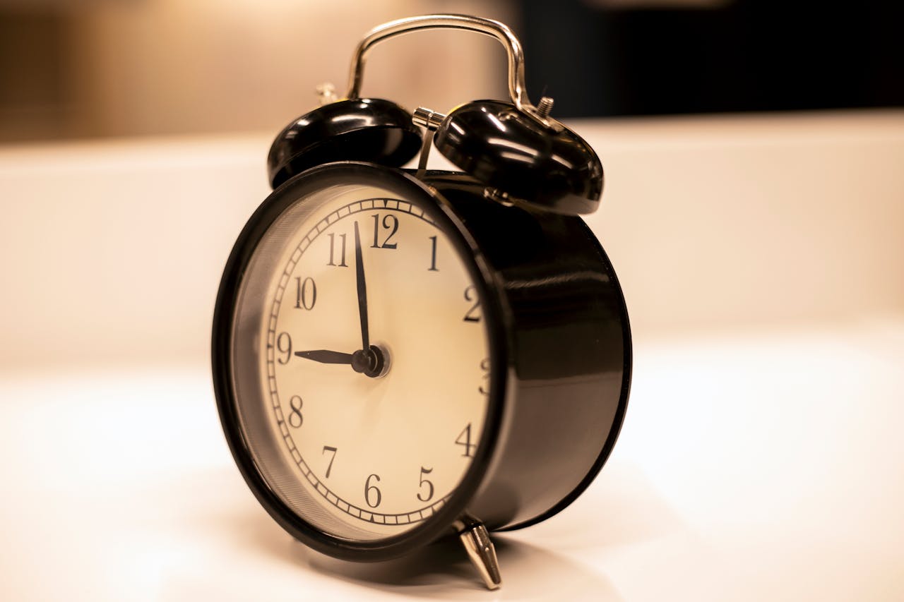 Services-01 Close-up of a classic black analogue alarm clock on a desk with a serene background.